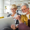 Mature couple reviewing investments and financial information on a laptop and tablet at home