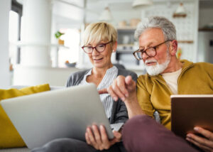 Mature couple reviewing investments and financial information on a laptop and tablet at home