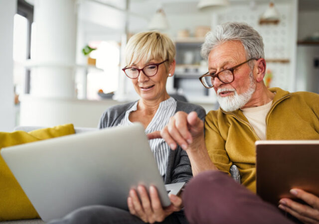 Mature couple reviewing investments and financial information on a laptop and tablet at home